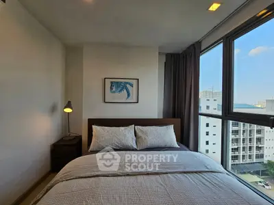 Cozy bedroom with large windows offering city views, modern decor, and ambient lighting.