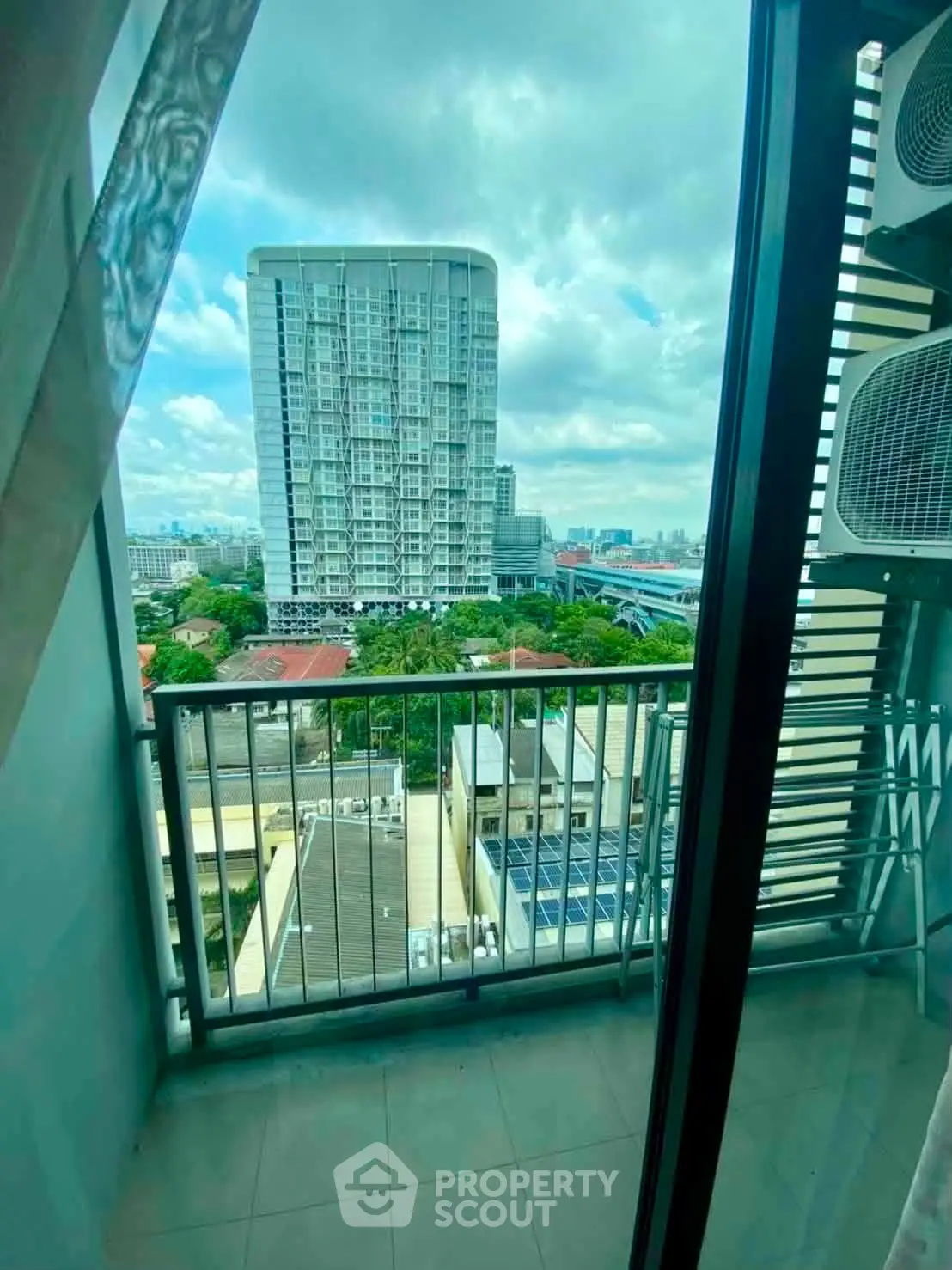 Stunning cityscape view from a modern apartment balcony with glass doors and lush greenery.