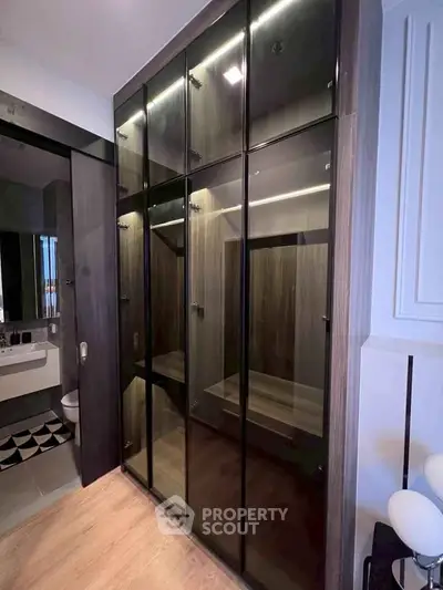 Modern bedroom with sleek glass wardrobe and en-suite bathroom, showcasing contemporary design and functionality.