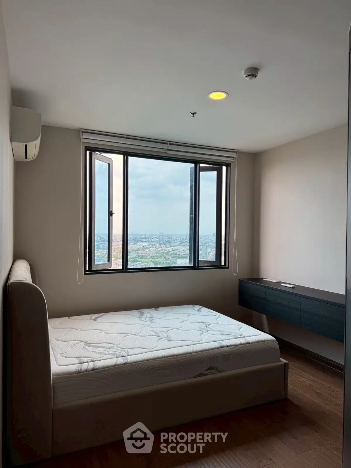 Spacious bedroom with large window offering stunning city views, featuring a comfortable bed and modern decor.