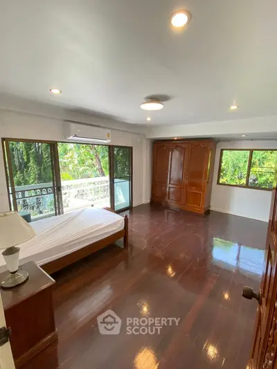 Spacious bedroom with hardwood floors and large windows overlooking greenery