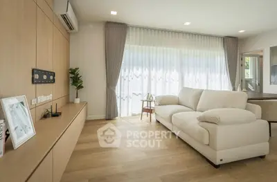 Modern living room with beige sofa, wooden flooring, and large window drapes.