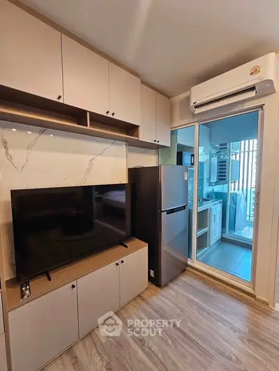 Modern living room with sleek TV unit and air conditioning, adjacent to a compact kitchen area.
