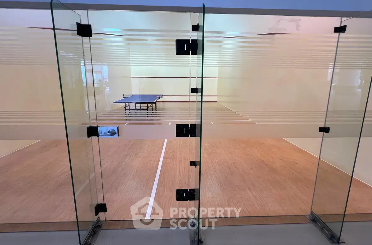 Modern indoor squash court with glass walls and a ping pong table, perfect for sports enthusiasts.