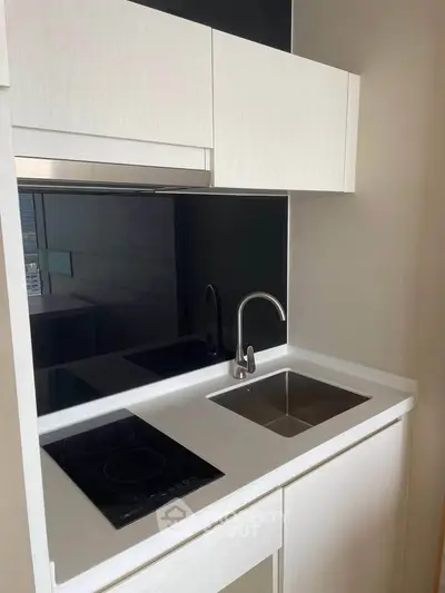 Modern compact kitchen with sleek white cabinetry and built-in electric cooktop.