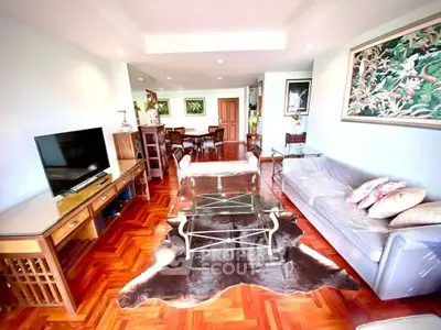 Spacious living room with elegant decor and hardwood flooring, featuring a stylish glass coffee table and modern TV setup.