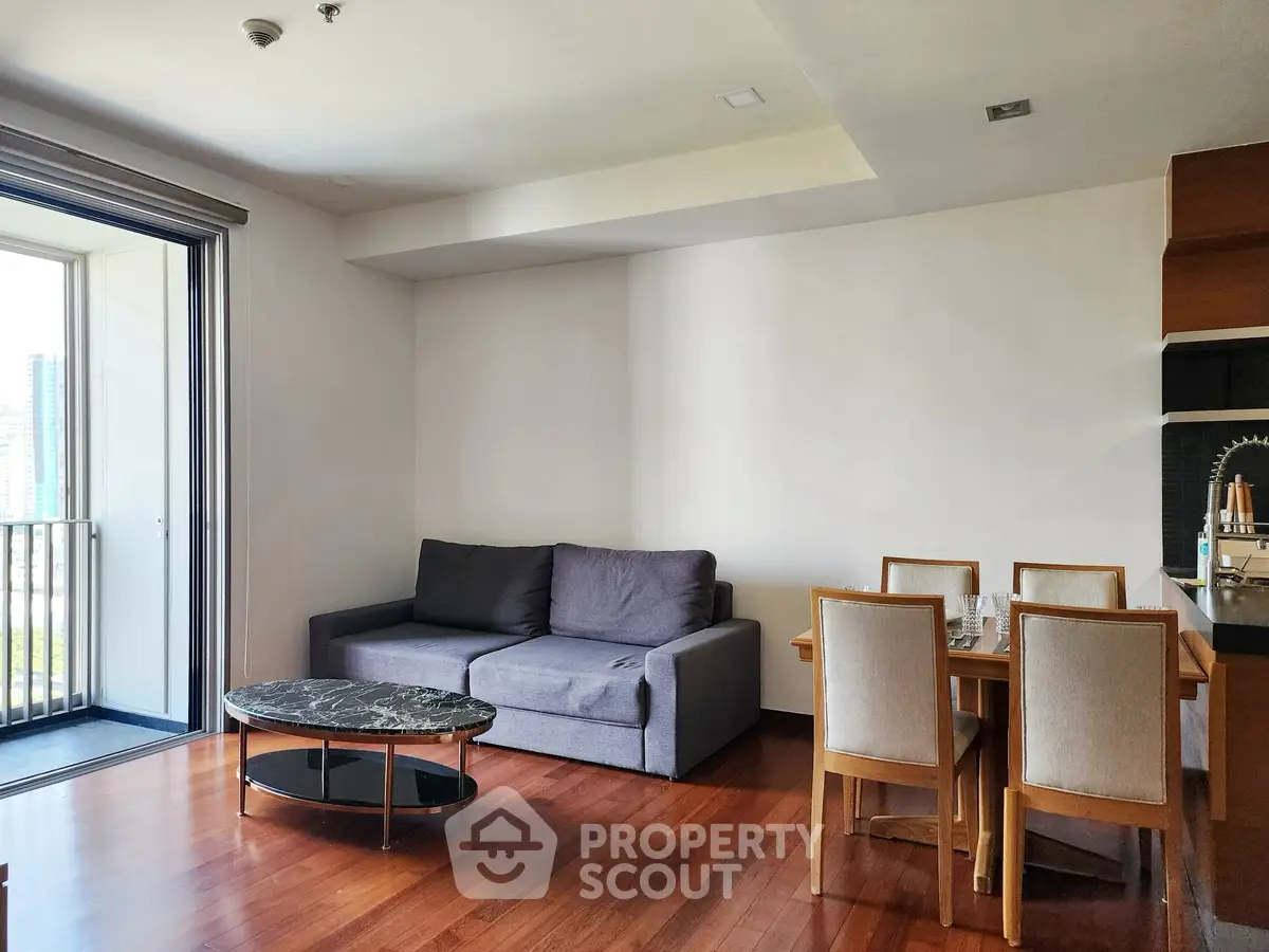 Modern living room with open balcony and dining area, featuring wooden flooring and contemporary furniture.