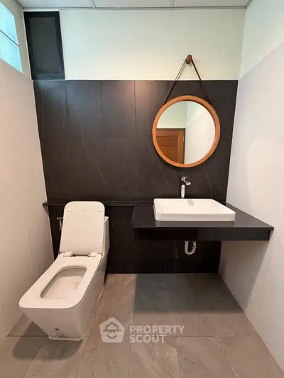 Modern bathroom with sleek design featuring a wall-mounted sink and round mirror.