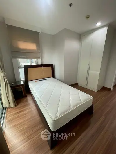 Modern bedroom with single bed, wooden flooring, and built-in wardrobe in a cozy apartment.