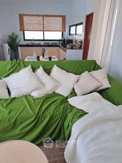 Cozy living room with green sofa, pillows, and open kitchen layout, perfect for modern living.
