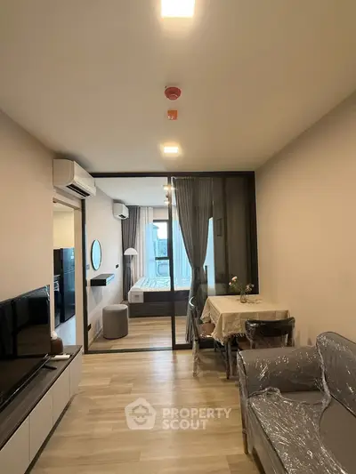 Modern apartment interior with open living area and bedroom, featuring sleek furniture and natural light.