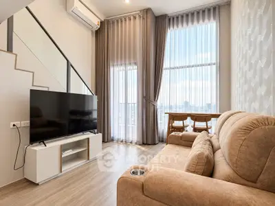 Modern living room with large windows, cozy sofa, and flat-screen TV, offering a bright and inviting atmosphere.