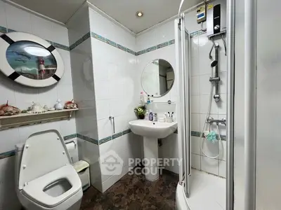 Compact modern bathroom with a corner shower cabin, pedestal sink, and toilet, accented with blue tile trim and mirrored accessories.