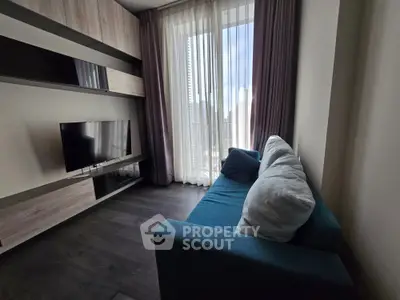 Modern living room with sleek TV setup and cozy blue sofa, featuring floor-to-ceiling windows for natural light.