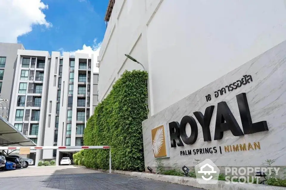 Modern condominium building exterior with lush greenery and clear blue sky.