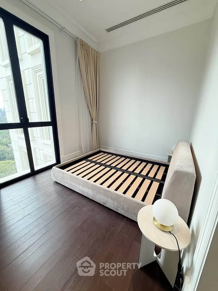Spacious bedroom with large window and modern bed frame in luxury apartment.