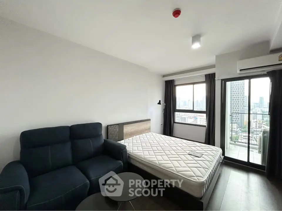 Modern studio apartment with city view, featuring a cozy bed, stylish sofa, and balcony access.