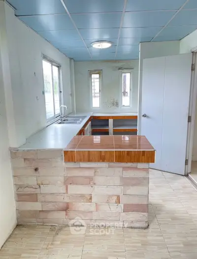 Spacious kitchen with open layout and natural light, featuring tiled countertops and modern fixtures.