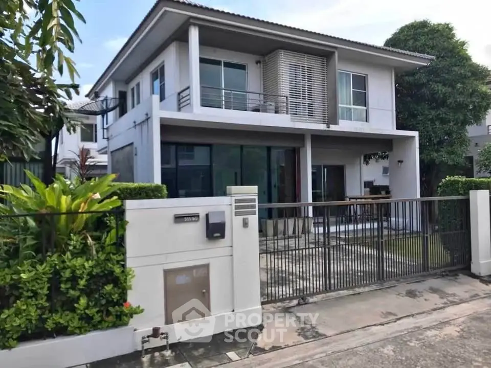 Modern two-story house with lush greenery and spacious balcony in a serene neighborhood.
