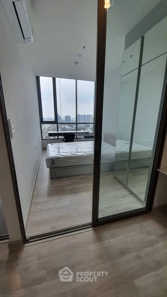 Modern bedroom with floor-to-ceiling windows offering stunning city views, featuring sleek design and ample natural light.