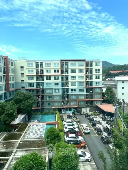 Modern apartment building with parking and lush greenery under a bright blue sky.