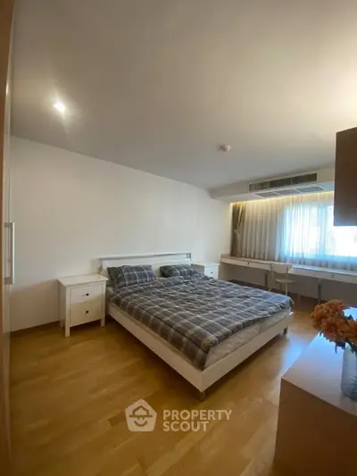 Spacious bedroom with wooden flooring and modern furnishings in a bright apartment.