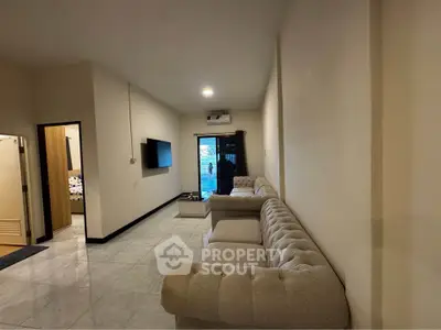 Spacious living room with elegant sofa and wall-mounted TV, leading to a balcony with a view.