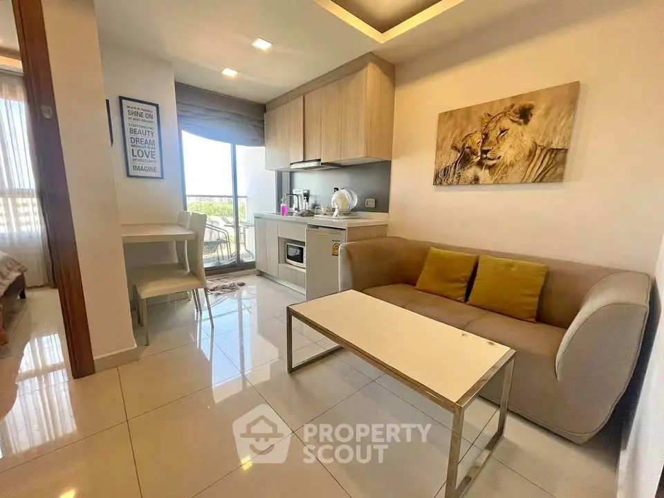 Modern open-layout living room with compact kitchen and cozy seating area, featuring a large window with natural light.