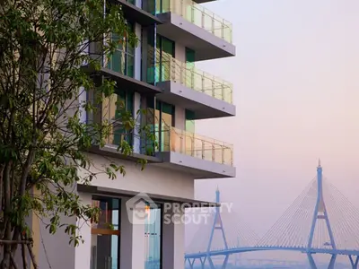 Modern apartment building with glass balconies and scenic bridge view at sunset.