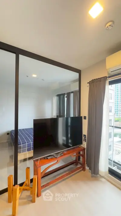 Modern apartment interior with glass partition, TV, and city view.
