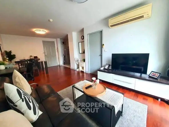 Spacious living room with modern decor and wooden flooring, featuring a cozy seating area and entertainment setup.