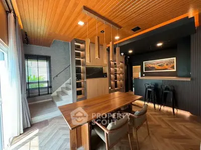 Modern living room with stylish wooden ceiling and open layout, featuring a dining area and sleek staircase.