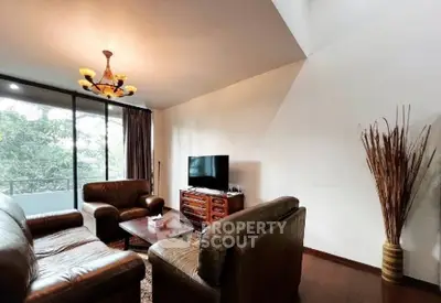 Spacious living room with leather sofas and large window offering lush green views.