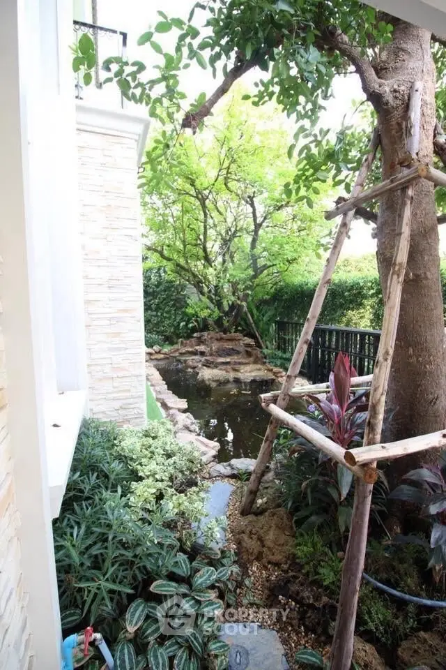 Charming garden view with lush greenery and serene pond in a residential setting.