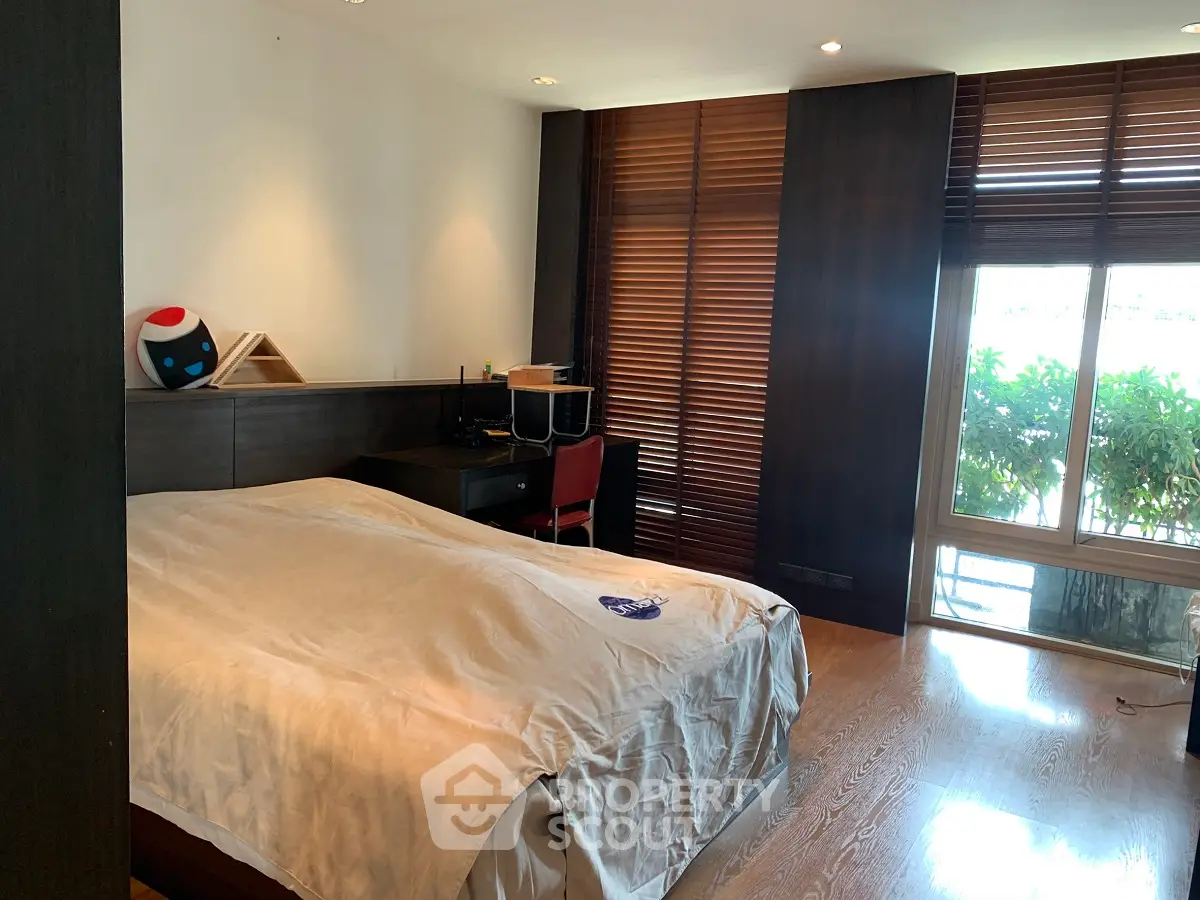 Spacious bedroom with large windows and wooden blinds, featuring a cozy workspace.