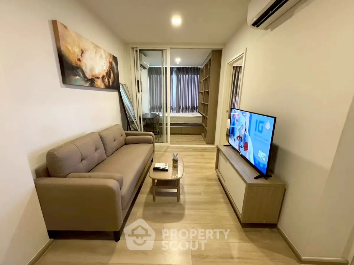 Modern living room with cozy sofa and TV, leading to a stylish bedroom through glass doors.