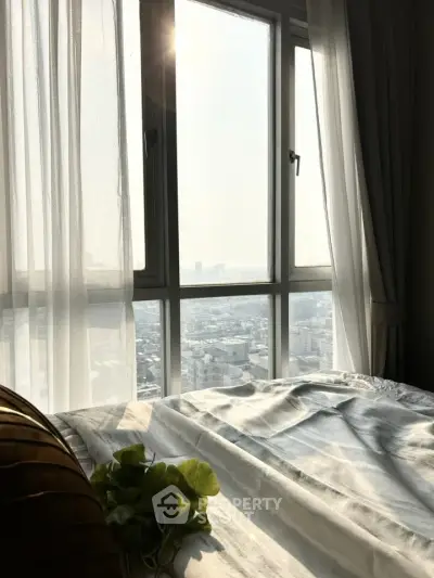 Bright bedroom with large window offering stunning city view, perfect for urban living.