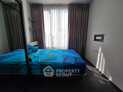 Modern bedroom with blue bedding and large window, featuring sleek design and ample natural light.
