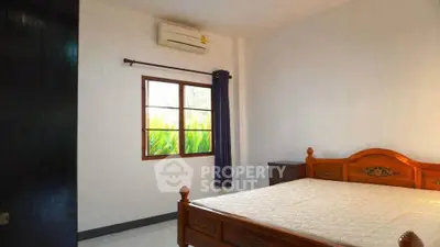 Cozy bedroom with wooden bed frame and window view of lush greenery.