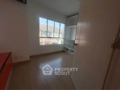 Bright bedroom with large window and built-in storage, showcasing natural light and modern flooring.
