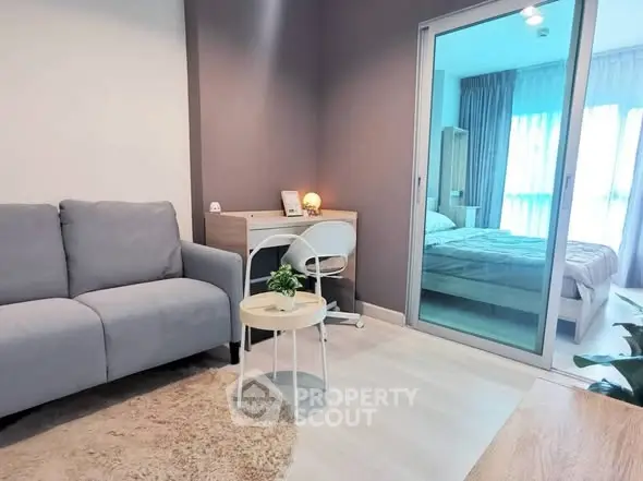 Modern living room with cozy sofa and study area leading to a bright bedroom.