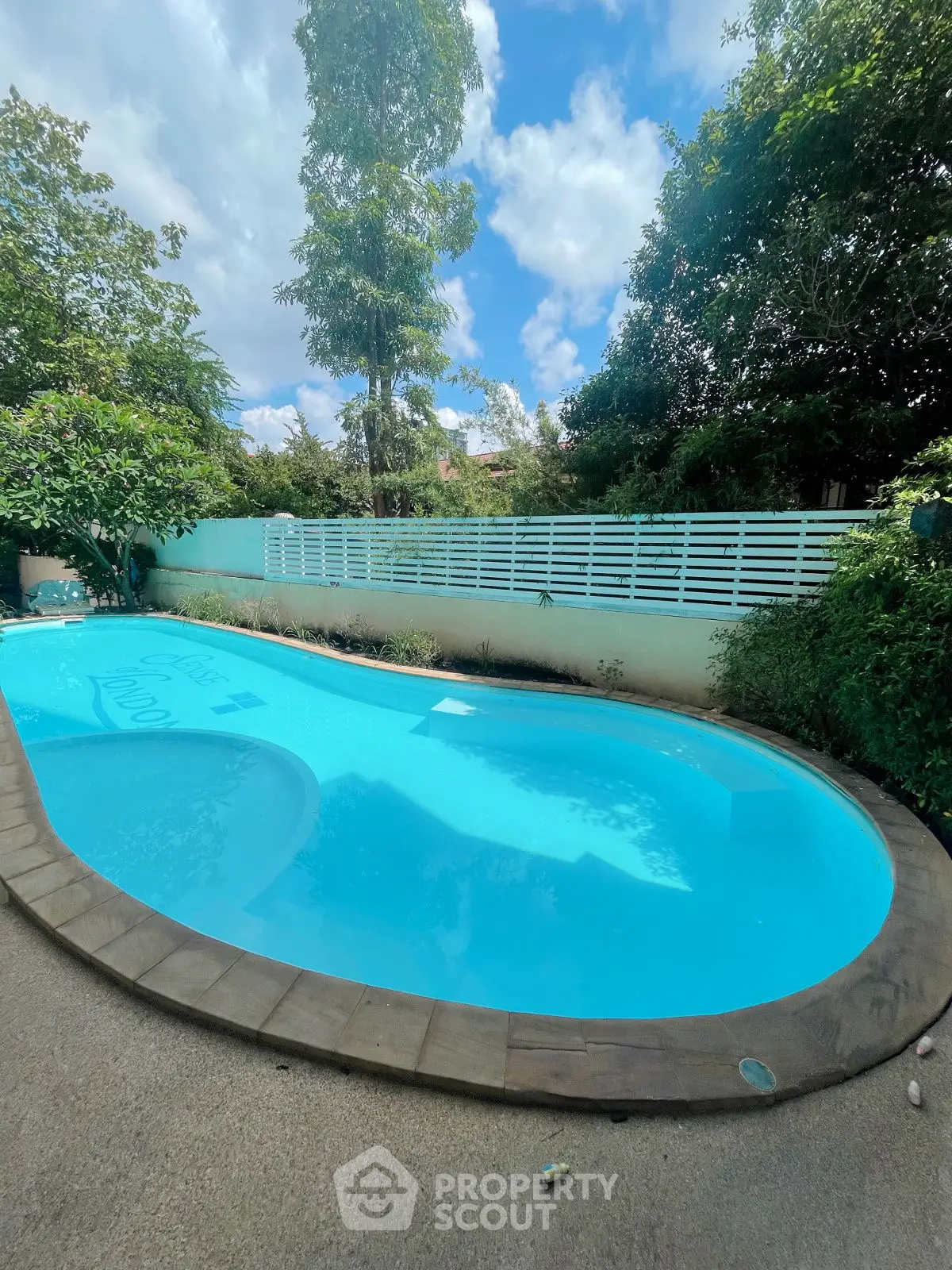 Stunning outdoor pool with lush greenery and clear blue skies, perfect for relaxation.