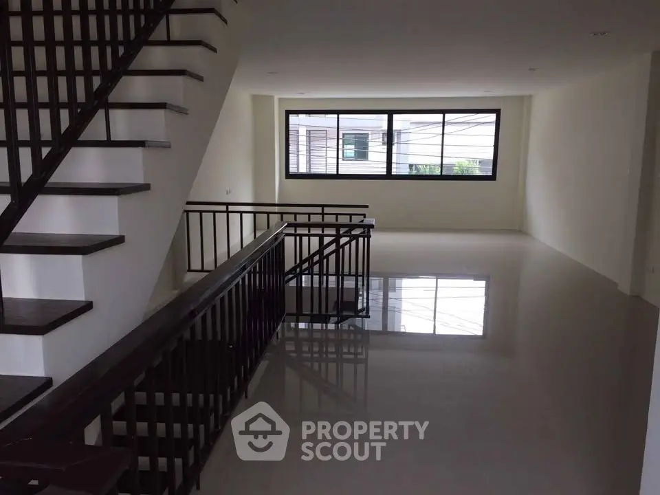 Spacious modern living room with sleek staircase and large window offering natural light.