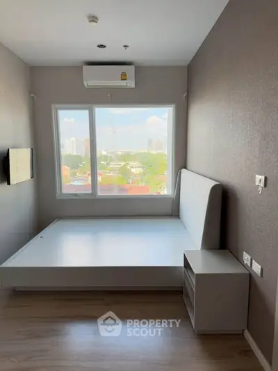 Modern bedroom with large window offering city view, featuring minimalist bed frame and air conditioning.