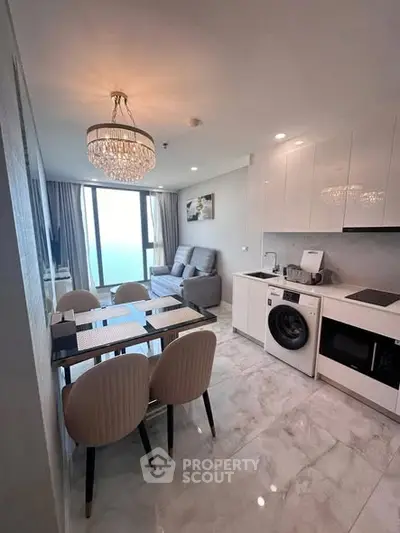 Modern open-plan living room with dining area and built-in appliances, featuring elegant chandelier and natural light.