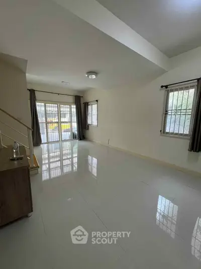 Spacious living room with large windows and glossy tiled floors in a modern home.