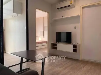 Modern living room with sleek furniture and open view to bedroom, featuring air conditioning and wooden flooring.