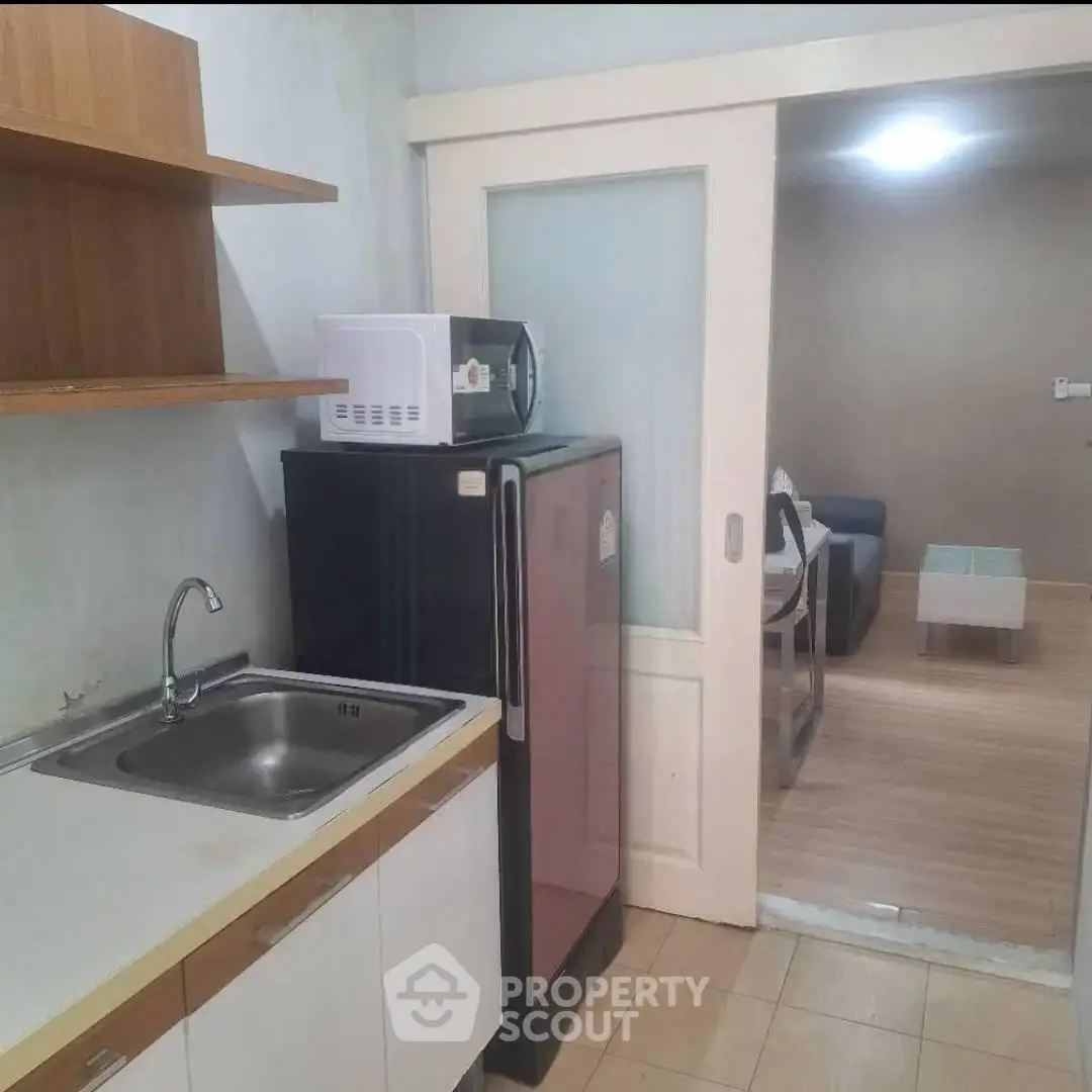 Compact kitchen with fridge and microwave leading to cozy living area