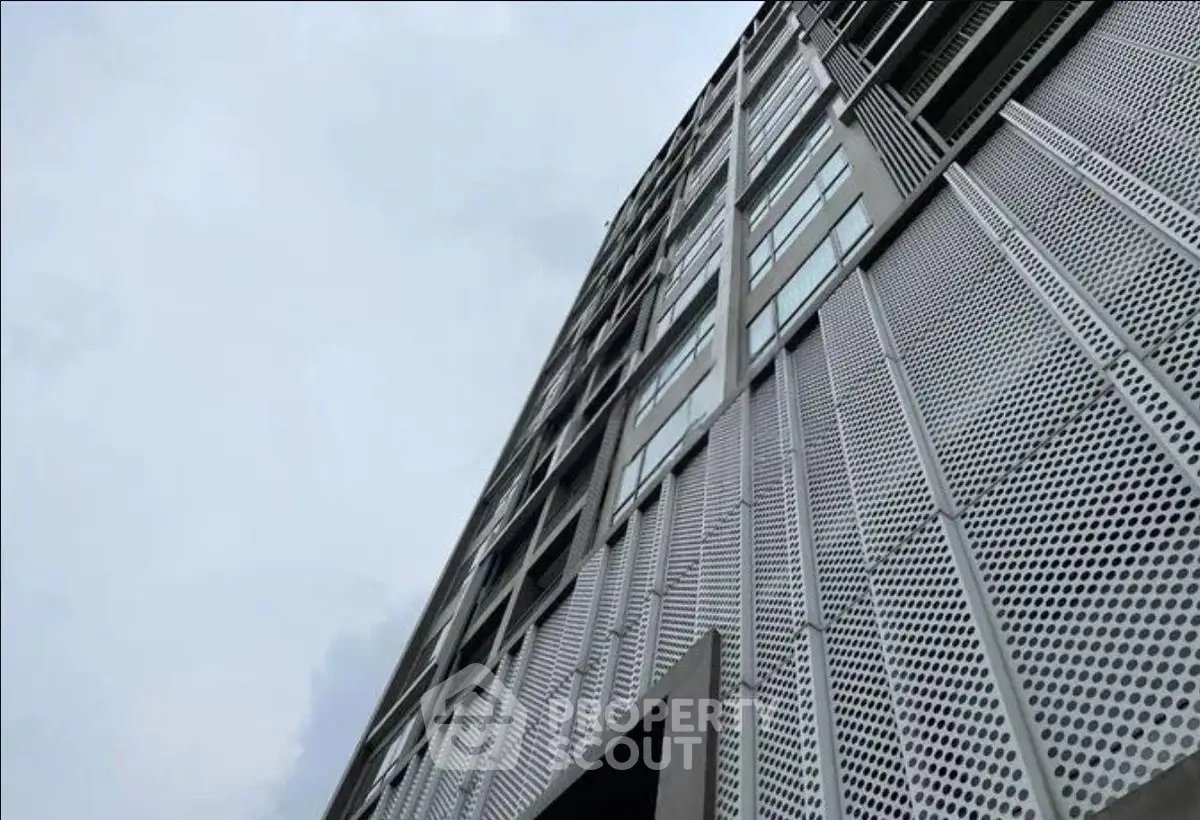 Modern high-rise building with unique perforated metal facade and large windows.