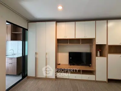 Modern living room with built-in cabinets and TV, adjacent to a sleek kitchen.